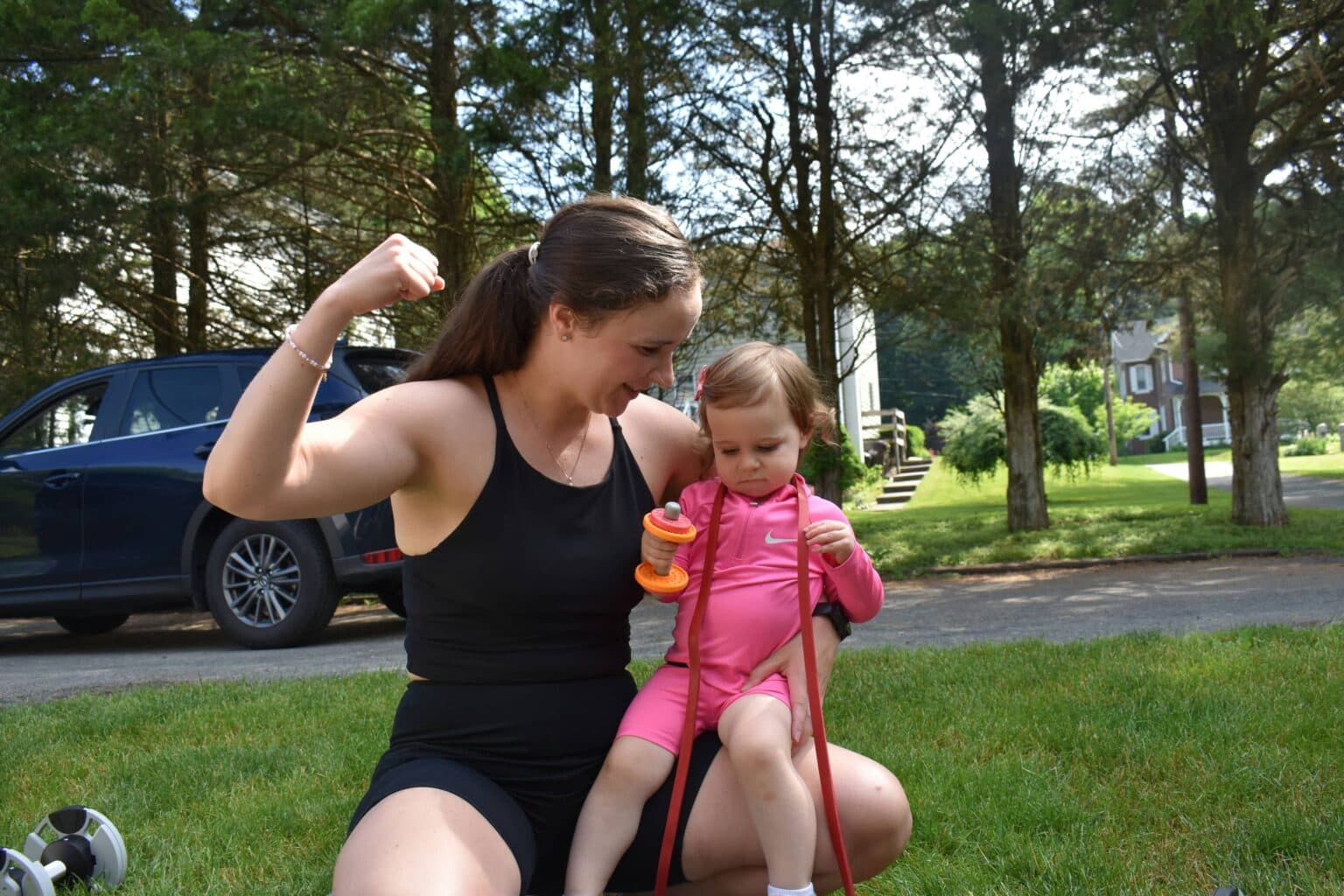 Lexi flexing her bicep next to her toddler holding a baby dumbbell